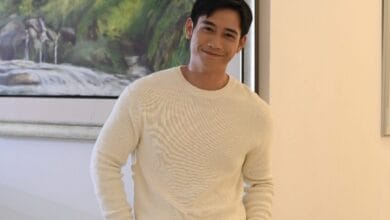 hun haqeem 2 - Wilayah.com.my Man in a white knit sweater smiles at the camera indoors, with a landscape painting on the wall behind him.