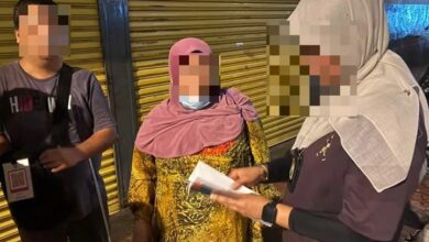 indonesia - Wilayah.com.my Three people stand near a yellow shutter; a woman in a pink headscarf holds papers as a man and another person listen, their faces blurred for privacy.