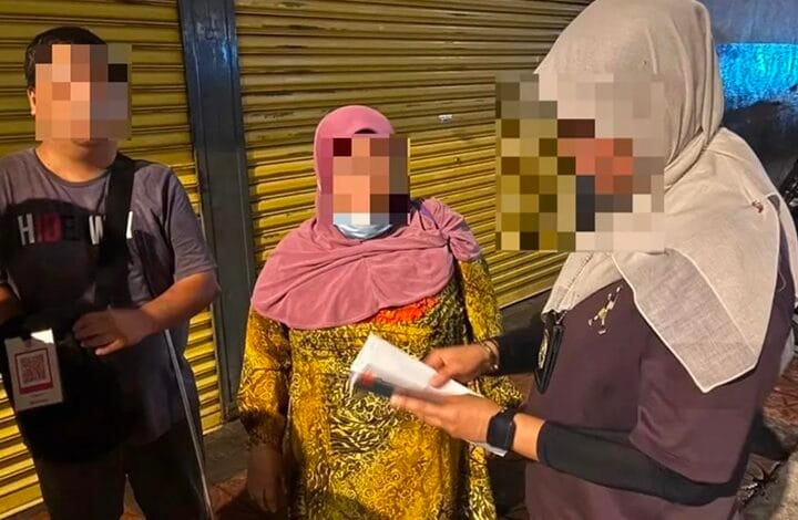 indonesia - Wilayah.com.my Three people stand near a yellow shutter; a woman in a pink headscarf holds papers as a man and another person listen, their faces blurred for privacy.
