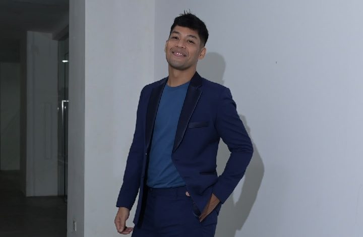 kamal adli - Wilayah.com.my Man in a navy suit with a blue shirt, smiling and standing against a white wall.