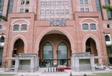 kdn - Wilayah.com.my Brick building with three arched entrances and a blue KDN sign; people near the doors and a red car in front.
