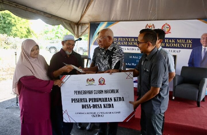 keda - Wilayah.com.my Group of people under a canopy participate in a ceremonial handover, presenting a large sign/banner to a man in a patterned shirt during a community housing grant event in Indonesia.