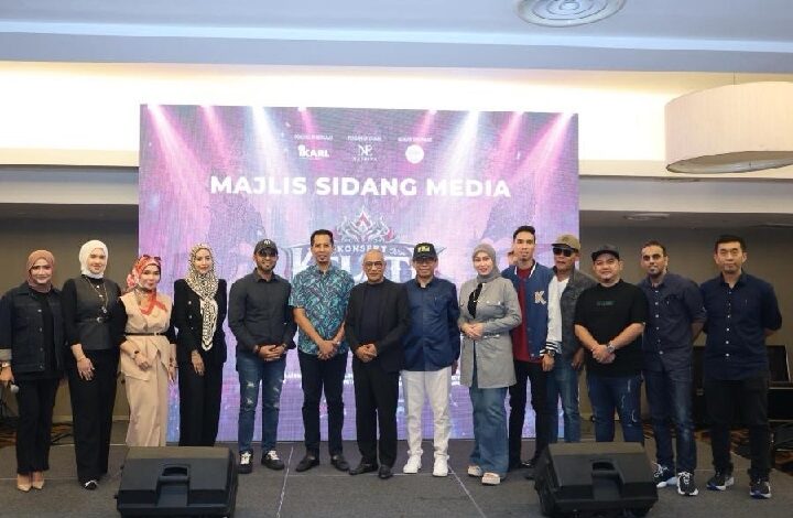 Group of men and women standing in a line on a stage in front of a purple backdrop that reads 'Majlis Sidang Media' during a media briefing.