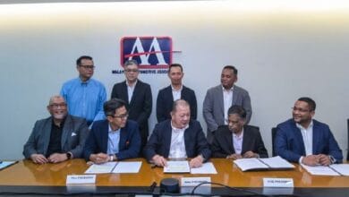 maa - Wilayah.com.my Eight men in business attire sit and stand around a conference table during a signing ceremony; documents and nameplates on the table, with a Malaysian Automotive Association logo on the wall behind them.