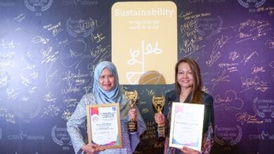 malakoff 2 - Wilayah.com.my Two women stand smiling, each holding a trophy and certificate at a sustainability awards backdrop.