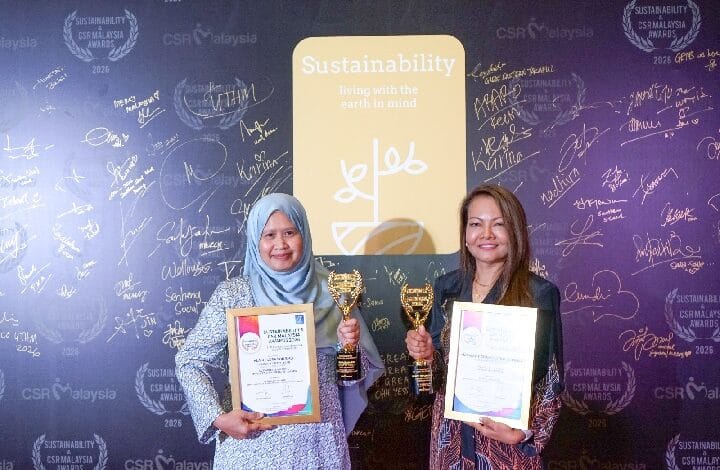 malakoff 2 - Wilayah.com.my Two women stand smiling, each holding a trophy and certificate at a sustainability awards backdrop.