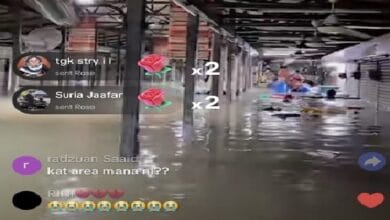 medan selera shah alam - Wilayah.com.my Livestream screenshot of a flooded warehouse with water on the floor, people in the background, and chat comments on the left with emoji reactions on the right.