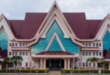 melaka - Wilayah.com.my Front view of a pink government building with steep gabled roofs and blue glass windows; entrance reads 'Jabatan Ketua Menteri Melaka'.