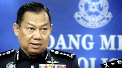 mohd faizal - Wilayah.com.my Senior police officer in dress uniform speaking at a press briefing, with ribbons on his chest and a blue backdrop featuring an official emblem