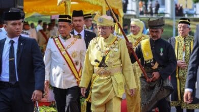 negeri sembilan - Wilayah.com.my Group of dignitaries in ornate ceremonial outfits walking on a red carpet; central figure wears gold attire and a crown.
