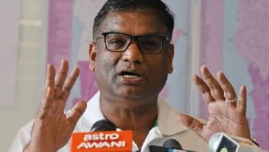 pathmanathan - Wilayah.com.my Man wearing glasses speaks at a press conference, with multiple microphones including Astro AWANI in front of him.