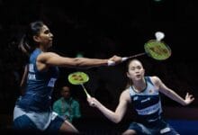 pearl thinaah - Wilayah.com.my Two female badminton players in blue uniforms stretch to return the shuttle during a doubles match.