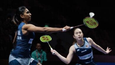 pearl thinaah - Wilayah.com.my Two female badminton players in blue uniforms stretch to return the shuttle during a doubles match.