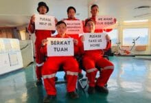 pelaut - Wilayah.com.my Five seafarers in red uniforms hold protest signs inside a ship’s cabin, calling for help, rights, and repatriation (Please help us; Please take us home). The messages include 'Malaysian Indonesian #Seafarer' and 'We want our right'.