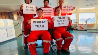 pelaut - Wilayah.com.my Five seafarers in red uniforms hold protest signs inside a ship’s cabin, calling for help, rights, and repatriation (Please help us; Please take us home). The messages include 'Malaysian Indonesian #Seafarer' and 'We want our right'.