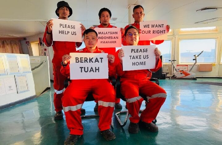 pelaut - Wilayah.com.my Five seafarers in red uniforms hold protest signs inside a ship’s cabin, calling for help, rights, and repatriation (Please help us; Please take us home). The messages include 'Malaysian Indonesian #Seafarer' and 'We want our right'.