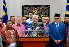 pembangkang 2 - Wilayah.com.my Group of Malaysian officials at a press conference behind a podium with multiple microphones, Parliament of Malaysia signage in the background and Malaysian flags on both sides.