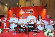 ph - Wilayah.com.my Six people stand behind a red table at a press conference, each holding a booklet titled 'Manifesto Harapan'.
