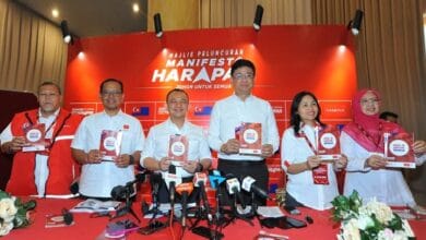 ph - Wilayah.com.my Six people stand behind a red table at a press conference, each holding a booklet titled 'Manifesto Harapan'.