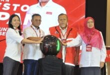 php pkr - Wilayah.com.my Four people in white shirts and red vests place their hands on a shiny black orb during a ceremony on a red-stage backdrop, signaling the event launch.