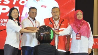 php pkr - Wilayah.com.my Four people in white shirts and red vests place their hands on a shiny black orb during a ceremony on a red-stage backdrop, signaling the event launch.