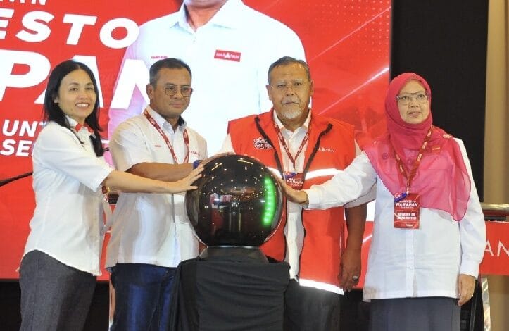 php pkr - Wilayah.com.my Four people in white shirts and red vests place their hands on a shiny black orb during a ceremony on a red-stage backdrop, signaling the event launch.