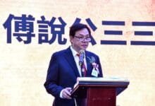 poh po lian - Wilayah.com.my Man in a dark suit and glasses giving a speech at a podium with a microphone, flower boutonniere, in front of a large Chinese character backdrop.