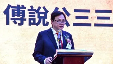 poh po lian - Wilayah.com.my Man in a dark suit and glasses giving a speech at a podium with a microphone, flower boutonniere, in front of a large Chinese character backdrop.