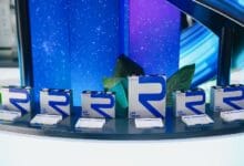 rept battero - Wilayah.com.my Row of blue-and-white product boxes with a large blue 'R' logo displayed on a curved display table, with green leaves in the background.