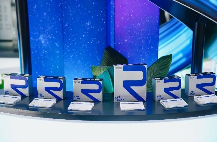 rept battero - Wilayah.com.my Row of blue-and-white product boxes with a large blue 'R' logo displayed on a curved display table, with green leaves in the background.