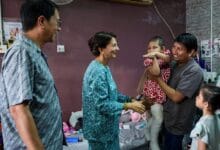 sarafudin badlishah - Wilayah.com.my Woman in teal outfit shakes hands with a man holding his child, as a girl watches in a casual family room setting.