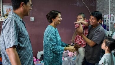 sarafudin badlishah - Wilayah.com.my Woman in teal outfit shakes hands with a man holding his child, as a girl watches in a casual family room setting.