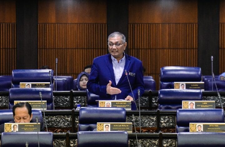 shamsul anuar - Wilayah.com.my Man in a blue blazer speaks at a podium in a formal council chamber with rows of blue seats and nameplates nearby (legislative setting).