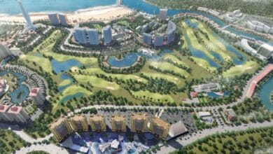 tanco - Wilayah.com.my Aerial view of a coastal resort with high-rise buildings, a marina, and a winding golf course surrounded by trees and water features.