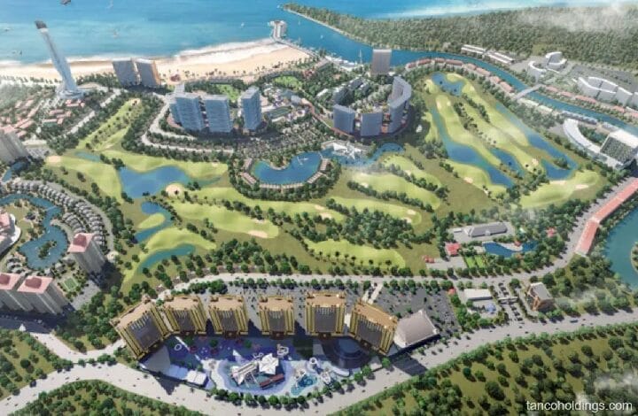 Aerial view of a coastal resort with high-rise buildings, a marina, and a winding golf course surrounded by trees and water features.