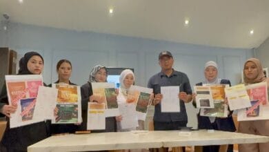 wan razila - Wilayah.com.my Eight people stand behind a table, each holding flyers and documents in a bright workshop room.