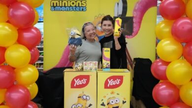 yeos - Wilayah.com.my Two women stand behind a yellow Minions & Monsters promotional booth with balloons on either side, smiling at the camera.