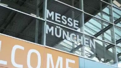 ztts - Wilayah.com.my Glass facade of the Messe München convention center with large 'MESSE MÜNCHEN' lettering and an orange 'WELCOME' banner.