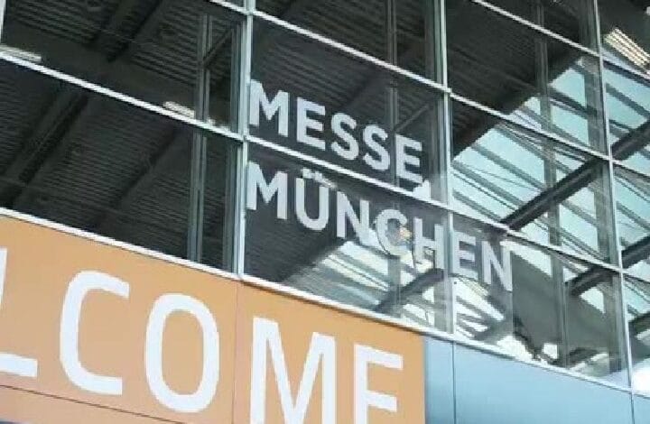 ztts - Wilayah.com.my Glass facade of the Messe München convention center with large 'MESSE MÜNCHEN' lettering and an orange 'WELCOME' banner.